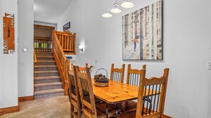 A dining area with a wooden table and chairs, a staircase, and a wall-mounted painting. - Moraine 1370 | Comfortable Mountain Townhome Near Steamboat Resort (Steamboat Springs)