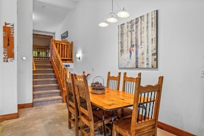 Uma área de refeições com mesa e cadeiras de madeira, uma escada e um quadro na parede.