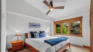 A bedroom with a bed, a nightstand, a lamp, a ceiling fan, a window with a view of greenery, and a framed picture on the wall. - Moraine 1370 | Comfortable Mountain Townhome Near Steamboat Resort (Steamboat Springs)