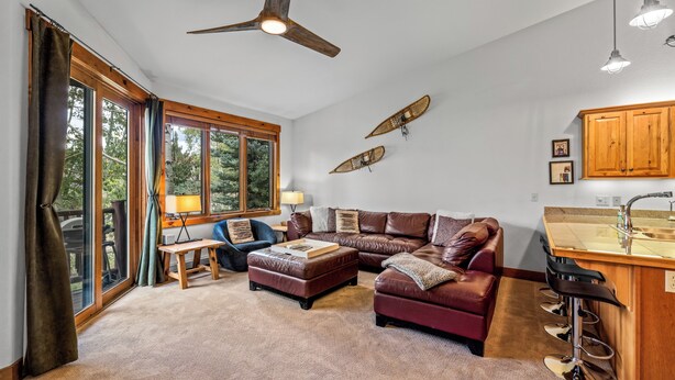 A spacious living area with a leather sofa, a small table, and a view of the outdoors through large windows. - Moraine 1370 | Comfortable Mountain Townhome Near Steamboat Resort (Steamboat Springs)