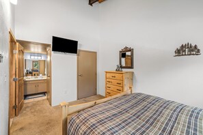 Un dormitori amb un llit, una petita taula de nit, una televisió i una porta que dona a un bany.