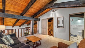 Ein geräumiger Raum mit hoher Holzbalkendecke, einem Holztisch, einer Couch und einer Treppe, die eine weitere Ebene hinaufführt.
