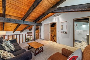 Una habitació àmplia amb un sostre de fusta alt, una taula de fusta, un sofà i una escala que condueix a un altre pis.