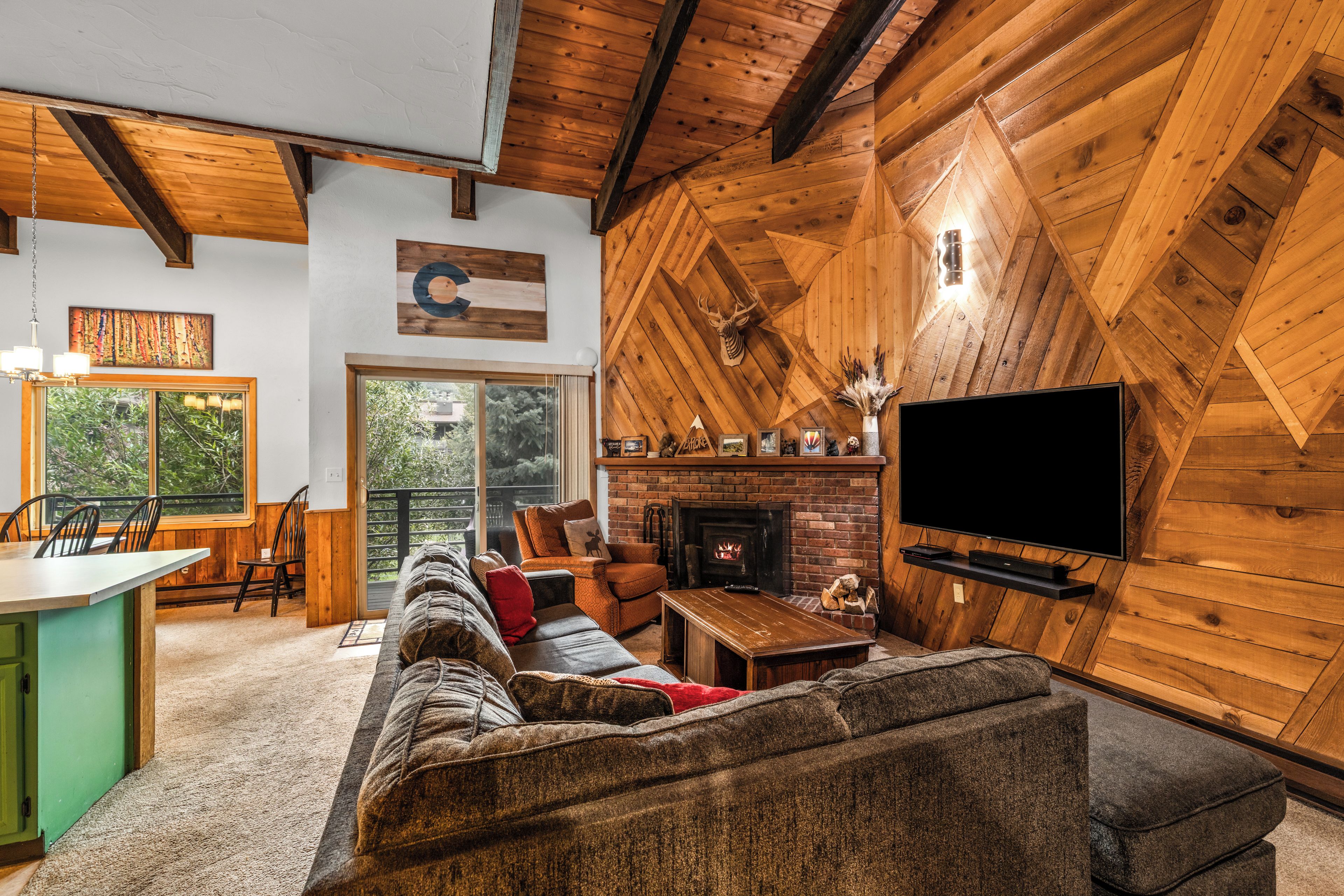 A cozy living room with a fireplace, a television, and a large window overlooking greenery.