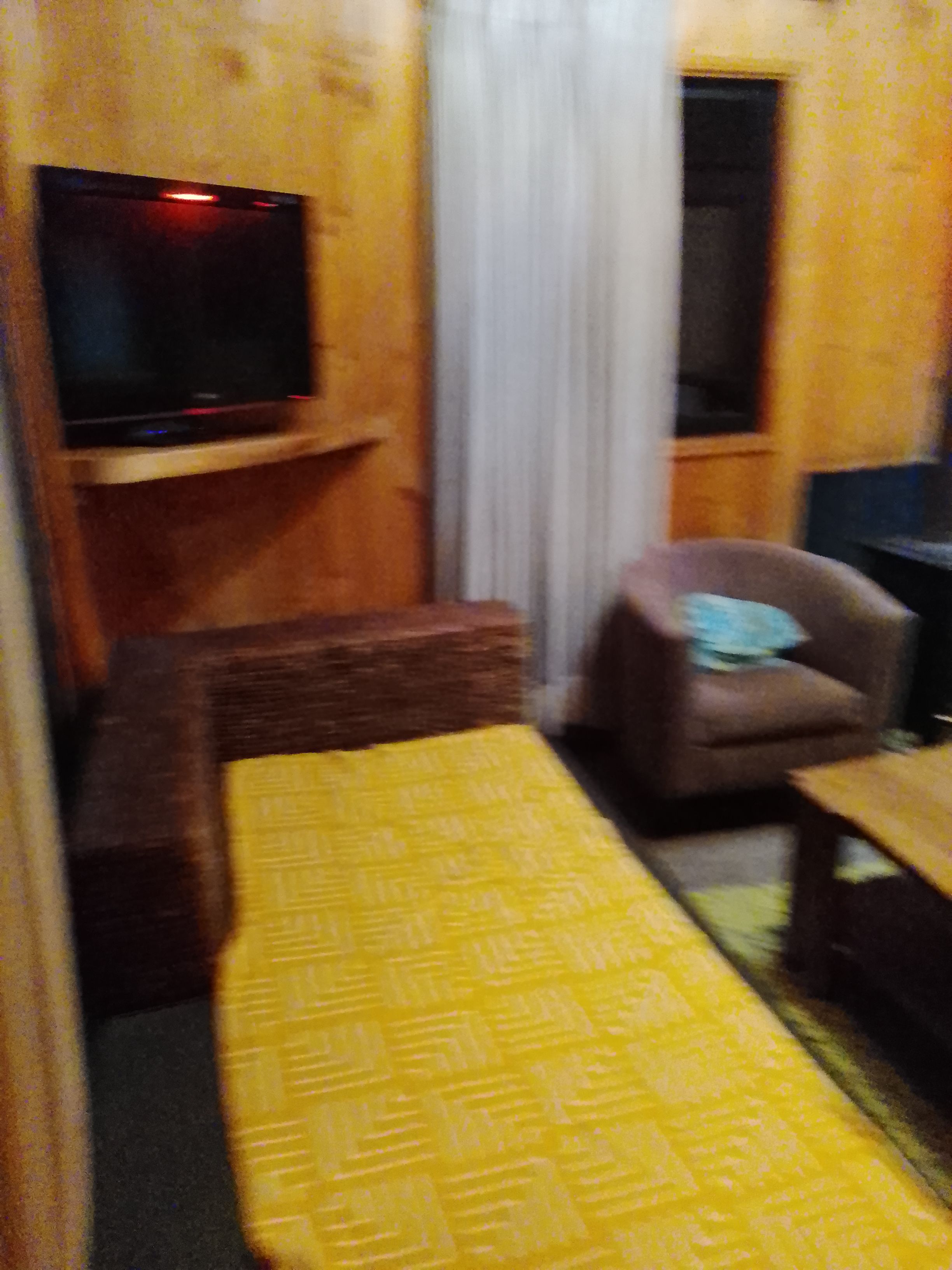 Ein Zimmer mit einem Bett, einem Fernseher auf einem Schrank, einem Sessel und einem kleinen Tisch.
