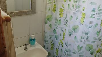 A bathroom with a white sink, a mirror, and a shower curtain with a leaf pattern.
