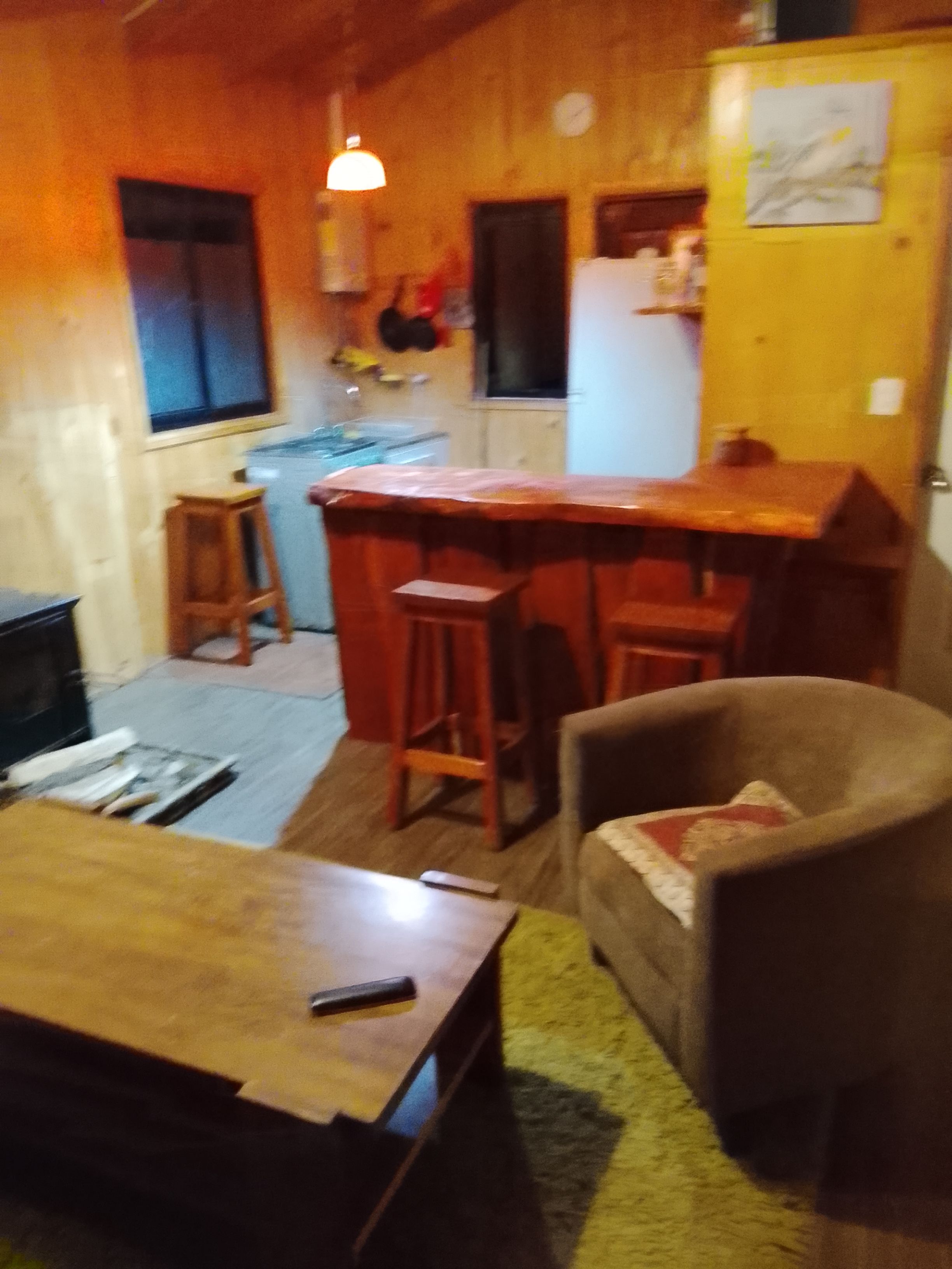 A cozy living room with a wooden coffee table, a comfortable armchair, and a kitchen area with a bar stool.