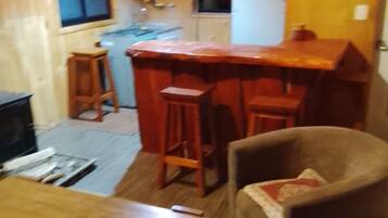 A cozy living room with a wooden coffee table, a comfortable armchair, and a kitchen area with a bar stool.