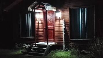 Edificio de madera con un porche y una puerta, iluminado por luces exteriores.