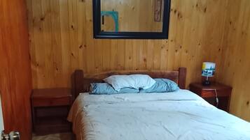 Una habitación con paneles de madera, una cama, una mesita de noche, una lámpara y una puerta.