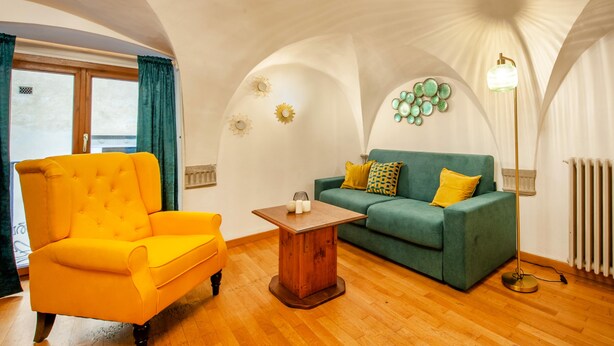 A room with a wooden floor, a yellow armchair, a green sofa with yellow cushions, a small wooden table, and a wall with decorative circular patterns. - In the Heart of Florence · 4 Min to Duomo & David (FIRENZE)