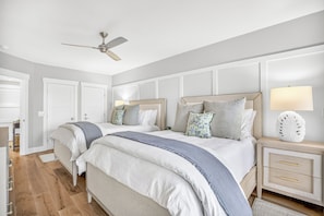 A bedroom with two beds, a ceiling fan, a bedside table with a lamp, and a nightstand with drawers. - Oceanfront, Updated, Open Plan & Super Stylish (Hilton Head Island)