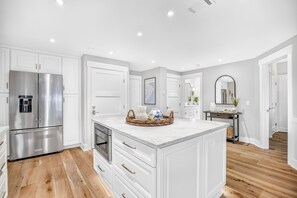 A modern kitchen with white cabinetry, a stainless steel refrigerator, a marble island, and wooden flooring. - Oceanfront, Updated, Open Plan & Super Stylish (Hilton Head Island)