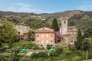 A traditional stone building with a tower, surrounded by lush greenery and a pool area. - Villa with natural spring amid Lucca vineyards (Lucca)
