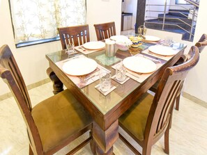 A dining table set with plates, glasses, and a bowl, surrounded by wooden chairs with cushioned seats. - Nakshatra Villa by Palette Homes 4bhk (Mawal)