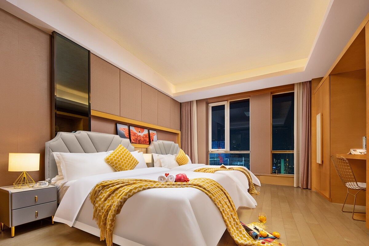 Quarto de hotel com uma cama grande, mesas de cabeceira, um criado-mudo, uma janela com vista e uma cadeira.