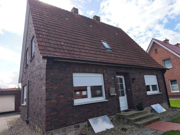 Ein Ziegelhaus mit rotem Ziegeldach, weißen Fensterläden und einer kleinen Veranda.