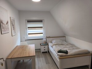 Ein Schlafzimmer mit einem Einzelbett, einem Nachttisch, einem Schreibtisch und einer Heizung.