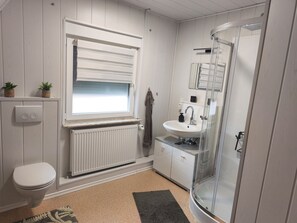 Ein Badezimmer mit Toilette, einem Fenster mit Jalousien, einem Waschbecken mit Spiegel und einer Duschkabine.