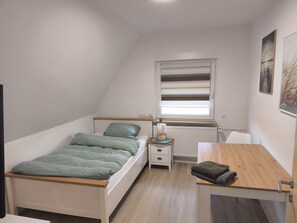 Ein kleiner, hell erleuchteter Raum mit einem Bett, einem Tisch und einem Fenster.