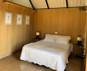 A bedroom with a large bed, wooden walls, and three framed pictures on the wall. - Chales Entre Vinhas (Canguera)