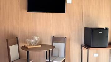 Una habitación con una mesa redonda, dos sillas, un televisor de pantalla plana en la pared y un refrigerador negro pequeño.