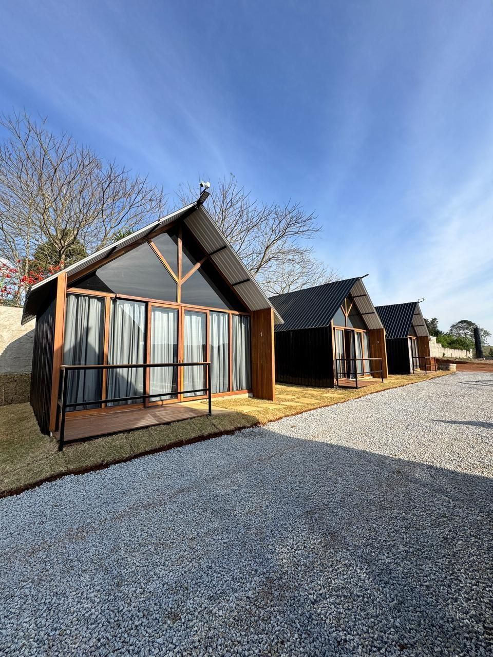 Fileira de cabanas modernas com janelas amplas e entrada por um caminho de cascalho.