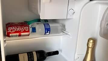 Un refrigerador abierto con una botella de champán, una botella de vino y una lata roja de Coca-Cola.