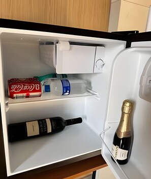 Un réfrigérateur ouvert contenant une bouteille de champagne, une bouteille de vin et une canette de Coca-Cola rouge.