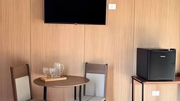 A room with a wooden wall, a flat-screen TV mounted above a table with two chairs, and a small black TV on a stand.