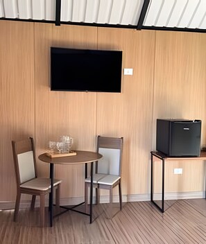 A room with a wooden wall, a flat-screen TV mounted above a table with two chairs, and a small black TV on a stand.