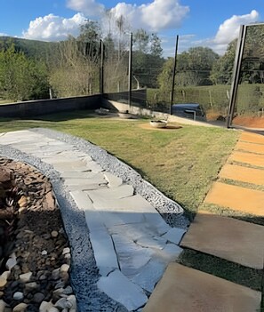 A landscaped outdoor area with a curved stone pathway, a grassy lawn, and a paved walkway. - Chales Entre Vinhas (Canguera)