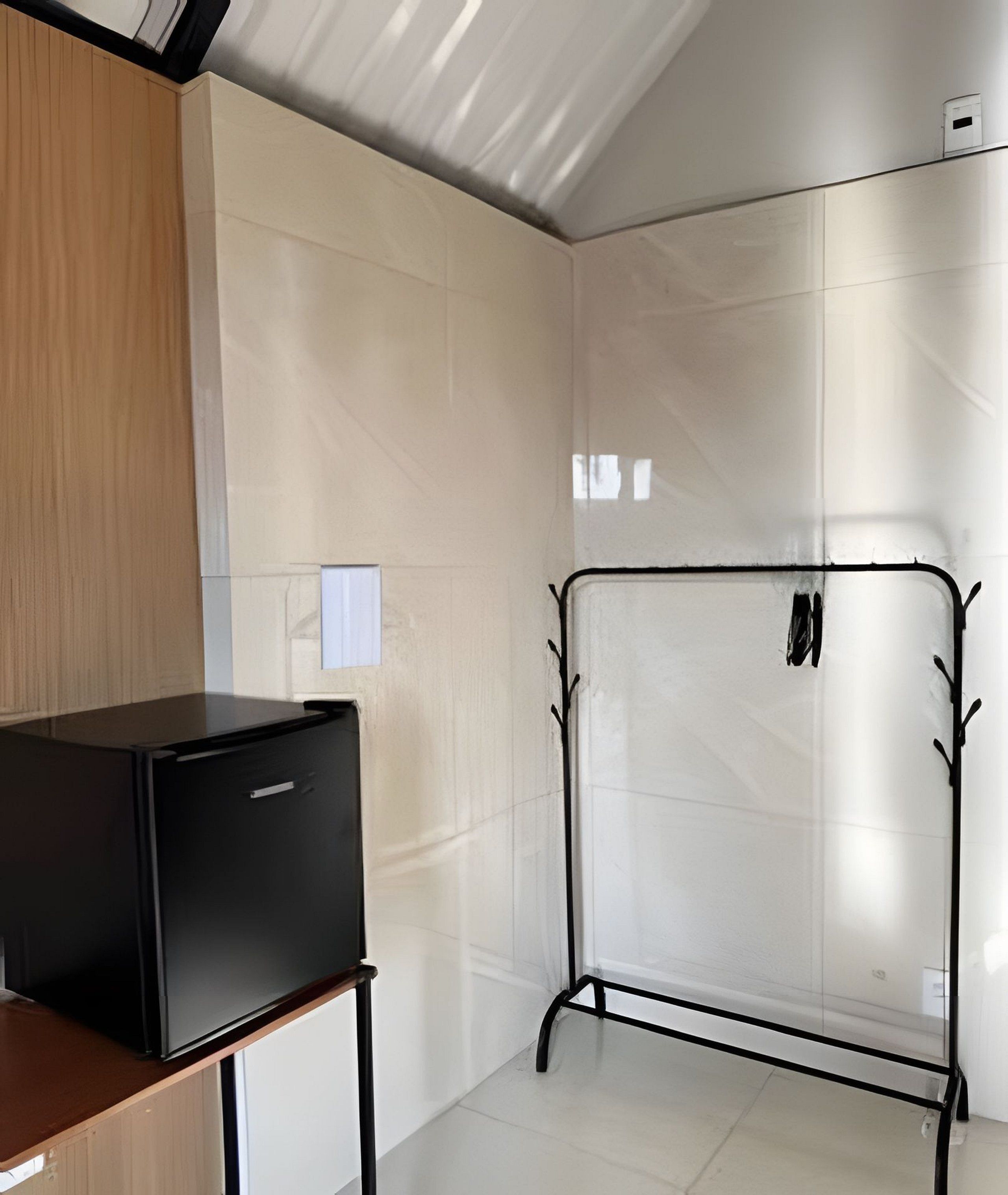 Una habitación con un calentador portátil negro sobre una mesa de madera, un perchero metálico con ganchos y una pared de azulejos.