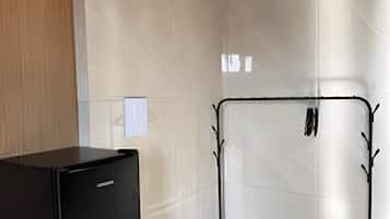 Una habitación con un calentador portátil negro sobre una mesa de madera, un perchero metálico con ganchos y una pared de azulejos.