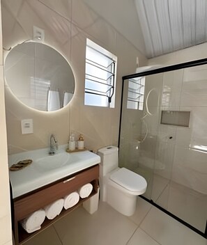 A modern bathroom with a glass-enclosed shower, a round mirror, and a vanity with a towel rack. - Chales Entre Vinhas (Canguera)