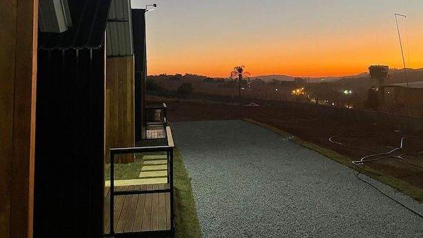 A pathway leading to a building with a dark exterior and a small outdoor seating area. - Chales Entre Vinhas (Canguera)