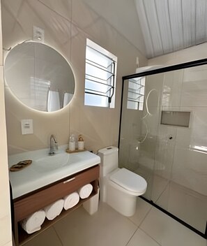 Un baño moderno con ducha envuelta en vidrio, un espejo redondo y un tocador con lavabo y perchero para toallas.
