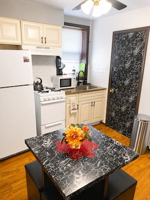 A kitchen with white cabinets, a stove, a microwave, and a sink. There is a table with a black marble top and a vase with flowers. - Compact Studio with AC and free street parking (Chicago)