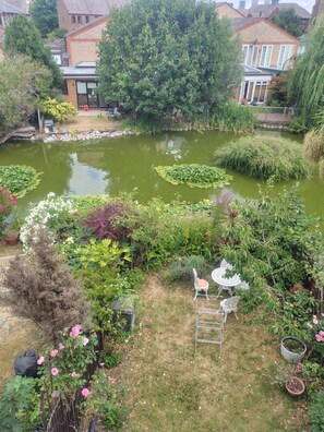 Ein Garten mit Teich, einem weißen Tisch und Stühlen im Freien sowie verschiedenen Pflanzen.