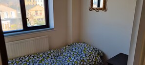Ein kleines Zimmer mit Fenster, Heizkörper und einem Bett mit gemustertem Überwurf.