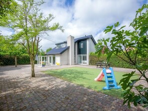 A residential property with a paved patio, a play area with a slide, and a house with a dark roof and large windows. - Holiday Home With 3 Bedrooms (De Cocksdorp)