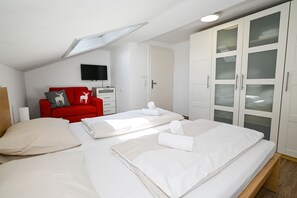 Un dormitorio moderno con tragaluz, un sofá rojo con cojines decorativos, un armario blanco y camas bien hechas.