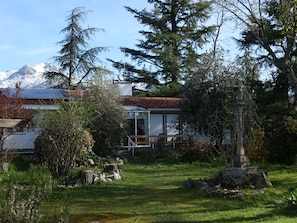 Uma casa com jardim, uma estátua de pedra e uma montanha ao fundo.