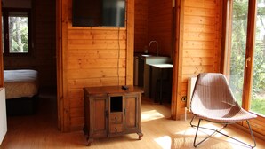Ein Holzblockhaus-Interieur mit einem Bett, einem Fernseher, einer kleinen Kommode, einem Waschbecken und einem Sessel.