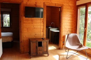 Interior de cabana de madeira com cama, televisão, armário pequeno, pia e uma cadeira.