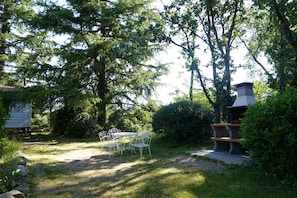 Um jardim com área de churrasqueira, mesa para piquenique e um pequeno galpão.