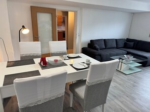 A modern living room with a dining area, a sofa, and a glass coffee table. - A Break in the Reinhardswald - Knickhagen Vacation Rental (Fuldatal)