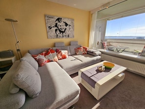 A living room with a sofa, a coffee table, and a window with a view. - Holiday Apartment With 1 Bedroom (Sierksdorf)