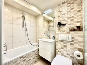 A bathroom with a bathtub, a sink, a mirror, and a toilet. - Holiday Apartment With 1 Bedroom (Sierksdorf)