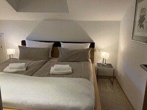 Ein Doppelbett mit zwei Kissen und zwei gefalteten Handtüchern, Nachttische mit Lampen und ein gerahmtes Bild an der Wand.